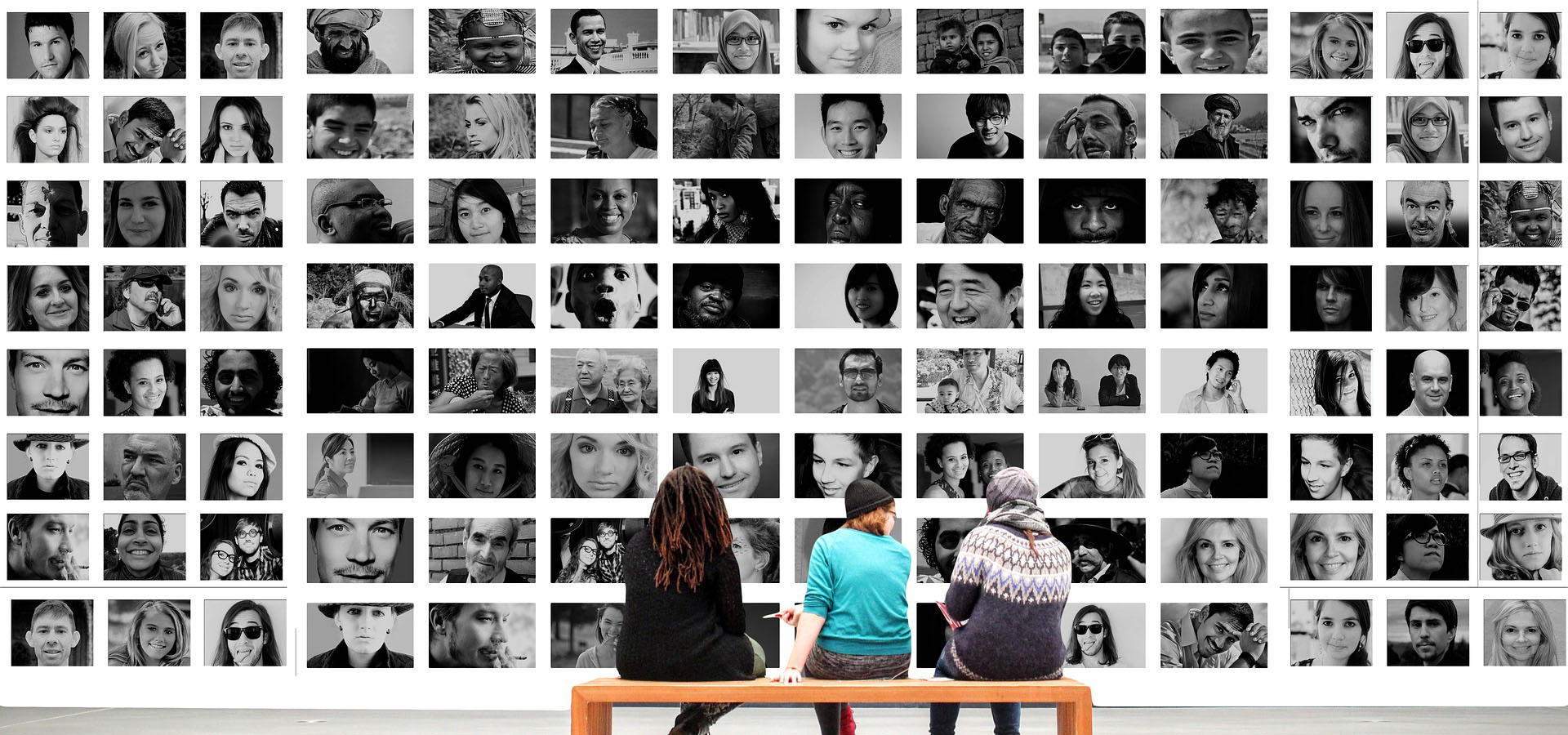 People sitting on bench and looking at wall of countless faces