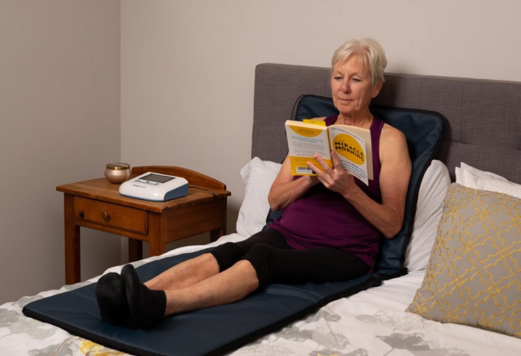 Woman in bed laying on PEMF Mat from BioBalance while reading