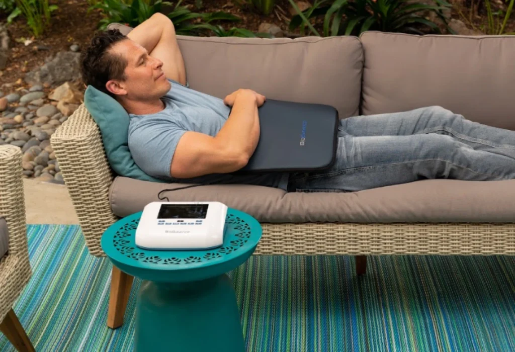 Man lying on outdoor couch with BioBalance PEMF Pillow on his lap