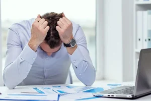 Man sitting at desk with computer open, pulling his hair as though he's stressed